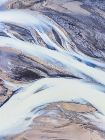 Aerial view of a braided glacial river with milky blue water flowing through dark volcanic sand deposits in Iceland. Aerial view of a braided glacial river with milky blue water flowing through dark volcanic sand deposits in Iceland.