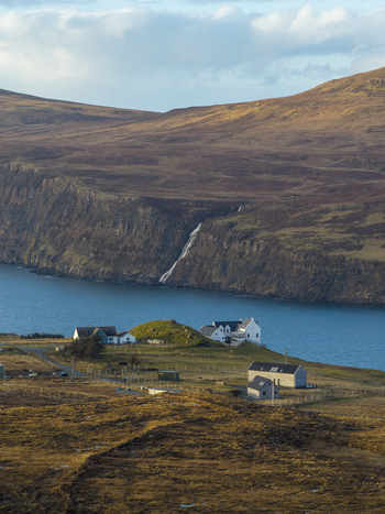 Aerial view of white houses on the green slopes overlooking the blue sea and a waterfall cascading down steep cliffs Milovaig Scotland United Kingdom.