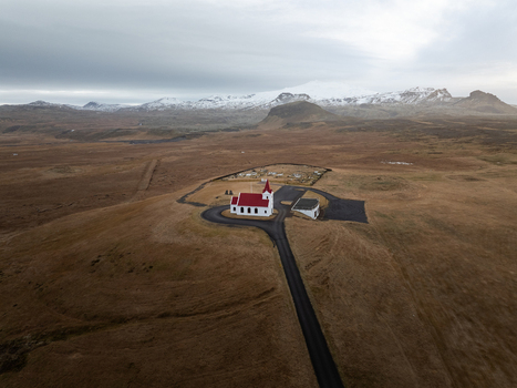 Aerial view of Ingjaldsholl Church with its distinctive red roof set against a vast hilly landscape and snow capped mountains in Hellissandur Snaefellsbaer Iceland. Aerial view of Ingjaldsholl Church with its distinctive red roof set against a vast hilly landscape and snow capped mountains in Hellissandur Snaefellsbaer Iceland.