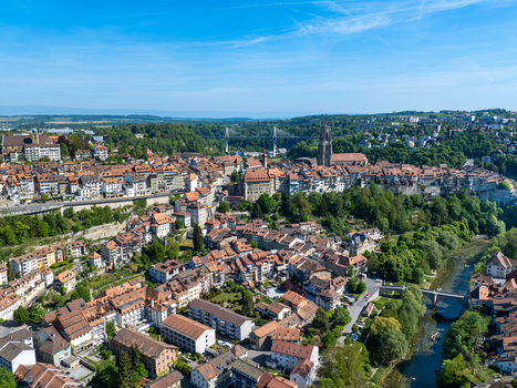 Aerial view of St Nicolas Cathedral and the historic old town with red tiled rooftops the Sarine river and the Poya Bridge under a clear blue sky in Fribourg Fribourg Switzerland. Aerial view of St Nicolas Cathedral and the historic old town with red tiled rooftops the Sarine river and the Poya Bridge under a clear blue sky in Fribourg Fribourg Switzerland.