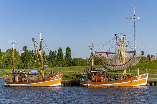 View of traditional Greetsiel fishing cutters with nets and rigging moored at the harbor under a clear blue sky in Krummhorn Lower Saxony Germany. View of traditional Greetsiel fishing cutters with nets and rigging moored at the harbor under a clear blue sky in Krummhorn Lower Saxony Germany.