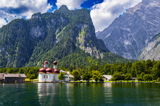 View of St. Bartholoma church with its red onion domes on the shore of Konigssee surrounded by lush forests and towering mountains in Schonau am Konigsee Bavaria Germany.