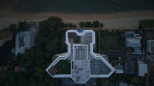 Aerial view of Jomtien Beach with a modern geometric building rooftop lush tropical trees and sandy shoreline Chon Buri Thailand.