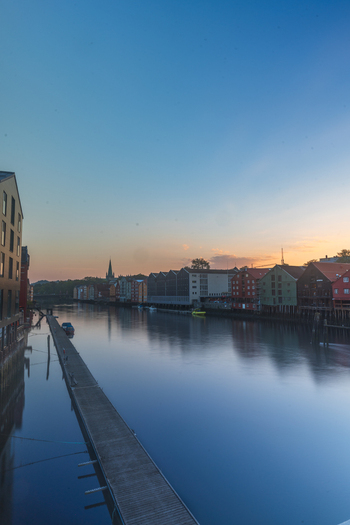 View of historic colorful wooden warehouses along the Nidelva river with calm water reflections and a distant cathedral spire at sunset Trondheim Trondelag Norway. View of historic colorful wooden warehouses along the Nidelva river with calm water reflections and a distant cathedral spire at sunset Trondheim Trondelag Norway.