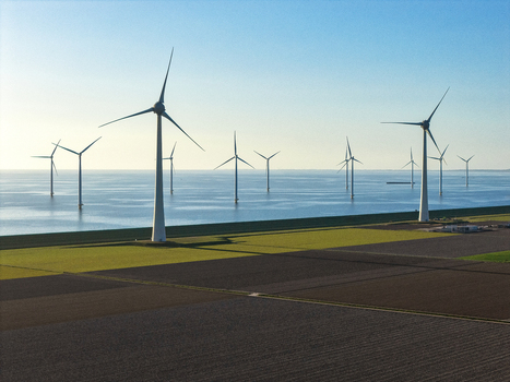 Aerial view of wind turbines standing in the sea and along the coastline next to agricultural fields under a clear blue sky Netherlands.