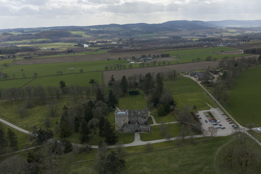 Aerial view of the historic Drum Castle surrounded by lush green lawns dense woodland and rolling hills under a cloudy sky in Drumoak Scotland United Kingdom.