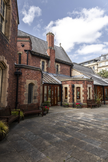 View of a historic red brick building with stone architectural details and a paved courtyard featuring wooden benches and potted flowers in Newcastle upon Tyne England United Kingdom. View of a historic red brick building with stone architectural details and a paved courtyard featuring wooden benches and potted flowers in Newcastle upon Tyne England United Kingdom.