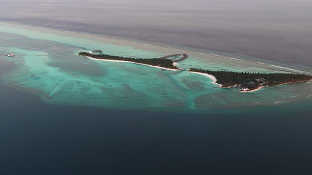 Aerial view of a tropical island and coral reefs in Maldives.