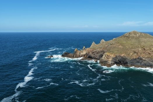 Aerial view of The Rumps a dramatic rocky headland on the coast with crashing waves and deep blue sea under a clear sky in Wadebridge England United Kingdom. Aerial view of The Rumps a dramatic rocky headland on the coast with crashing waves and deep blue sea under a clear sky in Wadebridge England United Kingdom.