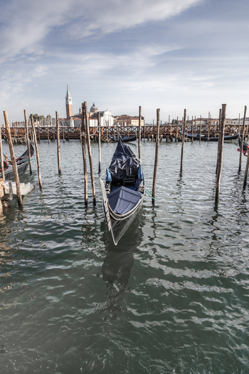 View of a traditional gondola moored to wooden pilings in the lagoon with the San Giorgio Maggiore church in the background in Venice Veneto Italy. View of a traditional gondola moored to wooden pilings in the lagoon with the San Giorgio Maggiore church in the background in Venice Veneto Italy.