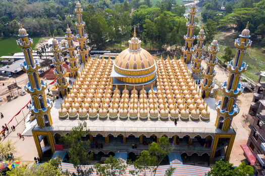 Aerial view of an intricately designed mosque its many golden domes and minarets gleaming brightly against the verdant surroundings Tangail Dhaka Division Bangladesh. Aerial view of an intricately designed mosque its many golden domes and minarets gleaming brightly against the verdant surroundings Tangail Dhaka Division Bangladesh.