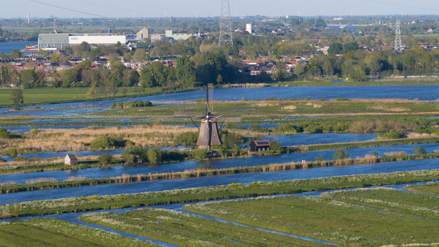 Aerial view of a historic windmill standing amidst a network of water canals and lush green polders under bright daylight Kinderdijk South Holland Netherlands. Aerial view of a historic windmill standing amidst a network of water canals and lush green polders under bright daylight Kinderdijk South Holland Netherlands.