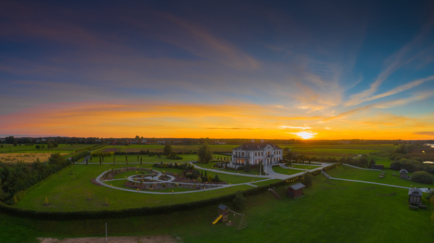 Aerial view of a grand manor house surrounded by manicured gardens green lawns and a small playground under a vibrant sunset sky in Latvia. Aerial view of a grand manor house surrounded by manicured gardens green lawns and a small playground under a vibrant sunset sky in Latvia.