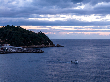 Aerial view of Getariako portua with a small fishing boat navigating the calm sea near the coastline of Getaria Basque Country Spain. Aerial view of Getariako portua with a small fishing boat navigating the calm sea near the coastline of Getaria Basque Country Spain.