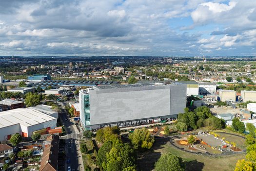 Aerial view of a modern data center building with a perforated facade surrounded by urban infrastructure industrial warehouses and a small park area in the United Kingdom. Aerial view of a modern data center building with a perforated facade surrounded by urban infrastructure industrial warehouses and a small park area in the United Kingdom.