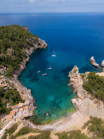 Aerial view of Cala Deia featuring turquoise waters rugged rocky cliffs and several boats anchored in the bay Spain. Aerial view of Cala Deia featuring turquoise waters rugged rocky cliffs and several boats anchored in the bay Spain.