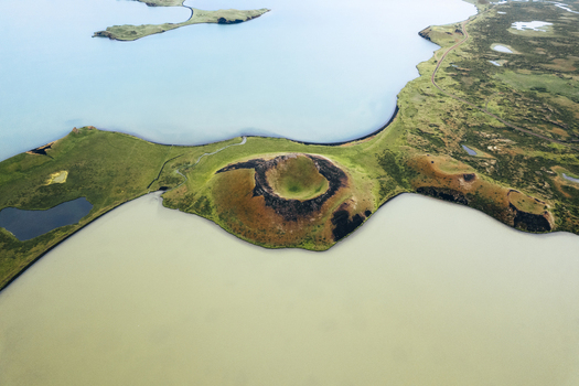Aerial view of contrasting turquoise and beige waters meet at the verdant shores near a volcanic crater creating an ethereal landscape Skutustadagigar Lake Myvatn Iceland.