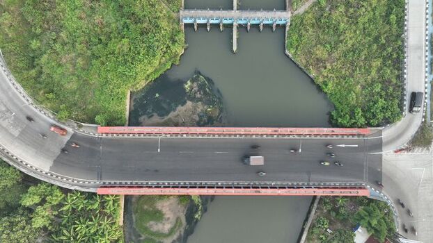 Aerial view of a bridge spanning a river with a sluice gate and traffic flowing across the asphalt road in Bekasi Barat West Java Indonesia. Aerial view of a bridge spanning a river with a sluice gate and traffic flowing across the asphalt road in Bekasi Barat West Java Indonesia.