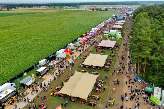 Herzogenaurach Germany 26 July 2025 Aerial view of the Open Beatz Festival grounds featuring large tents food stalls and crowds of people surrounded by lush green fields.