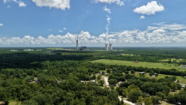 Aerial view of the Seminole Electric power plant with its cooling towers and smoke stacks rising above the surrounding lush green forest landscape in Palatka Florida United States.