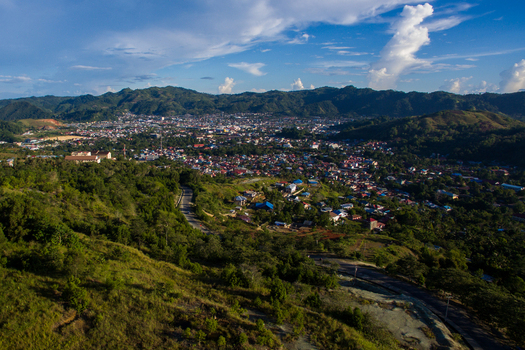Aerial view of the urban landscape of Jayapura nestled between lush green hills and mountains under a blue sky with white clouds in Jayapura Papua Indonesia.