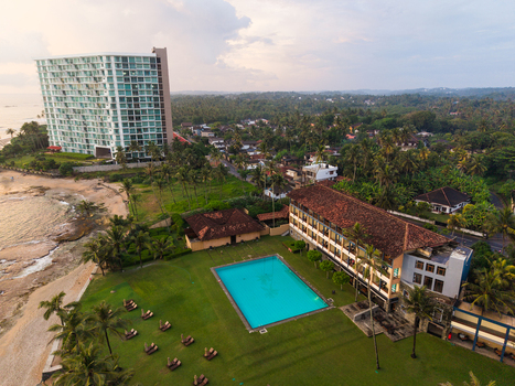 Aerial view of Gintota beach featuring a large swimming pool a modern high rise hotel and lush palm trees along the coast in Galle Southern Province Sri Lanka. Aerial view of Gintota beach featuring a large swimming pool a modern high rise hotel and lush palm trees along the coast in Galle Southern Province Sri Lanka.