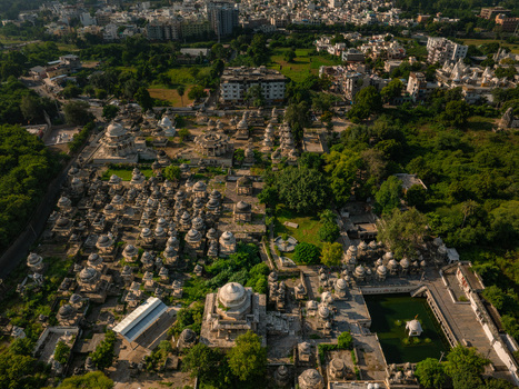 Aerial view of the historic Ahar Cenotaphs featuring numerous stone domes and monuments surrounded by lush greenery and a water tank in Udaipur Rajasthan India.
