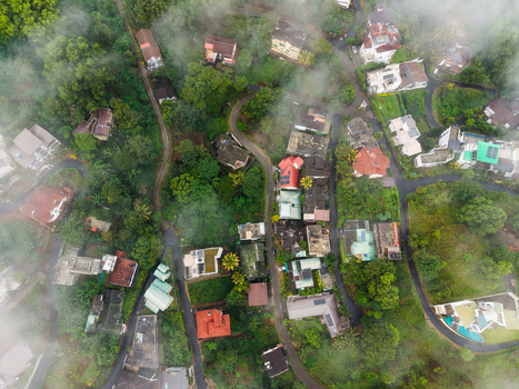 Aerial view of houses nestled among lush tropical greenery and winding roads partially covered by morning mist Kandy Central Province Sri Lanka. Aerial view of houses nestled among lush tropical greenery and winding roads partially covered by morning mist Kandy Central Province Sri Lanka.
