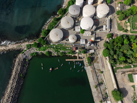 Aerial view of an industrial facility with large white storage tanks a small harbor with boats and a breakwater along the coast in Bajos de Haina San Cristobal Province Dominican Republic.