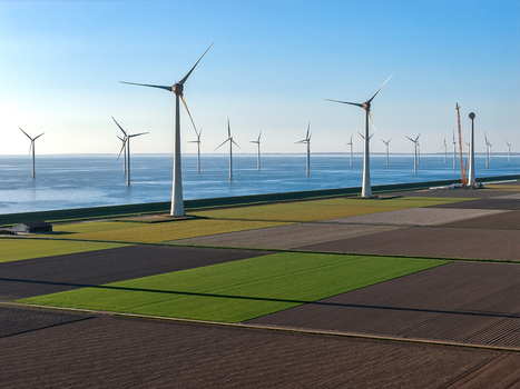 Aerial view of wind turbines standing in agricultural fields and along the coastline under a clear blue sky Netherlands.