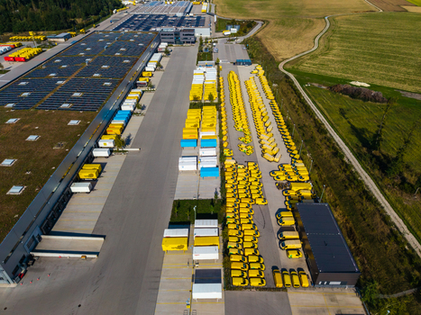 Aerial view of Logistikzentrum Allhaming featuring rows of yellow delivery vans a large warehouse with solar panels on the roof and surrounding fields in Allhaming Oberosterreich Austria. Aerial view of Logistikzentrum Allhaming featuring rows of yellow delivery vans a large warehouse with solar panels on the roof and surrounding fields in Allhaming Oberosterreich Austria.