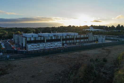 Aerial view of a modern data center facility with industrial buildings cooling units on the roof and a fenced perimeter during golden hour in United Kingdom. Aerial view of a modern data center facility with industrial buildings cooling units on the roof and a fenced perimeter during golden hour in United Kingdom.