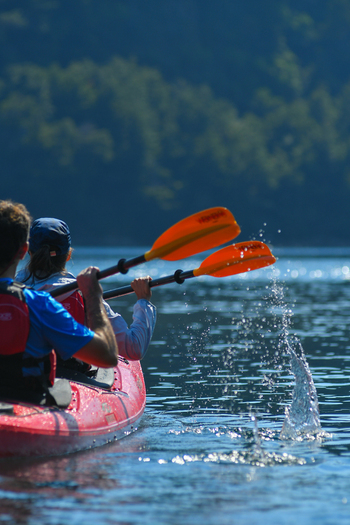 View of people paddling a red kayak on the blue waters of Nahuel Huapi Lake with forested hills in the background San Carlos de Bariloche Rio Negro Argentina. View of people paddling a red kayak on the blue waters of Nahuel Huapi Lake with forested hills in the background San Carlos de Bariloche Rio Negro Argentina.