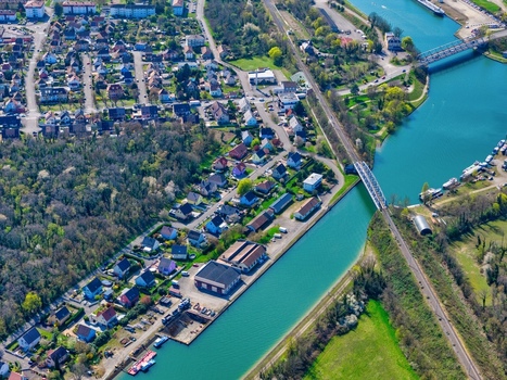 Aerial view of the tranquil canal reflecting the sky s soft hues contrasting with the terracotta roofs and the verdant trees near the houses Sausheim Grand Est France.