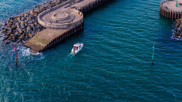 Aerial view of a small motorboat navigating the harbor entrance at West Bay featuring stone piers deep blue water and coastal infrastructure in West Bay England United Kingdom. Aerial view of a small motorboat navigating the harbor entrance at West Bay featuring stone piers deep blue water and coastal infrastructure in West Bay England United Kingdom.