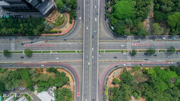 Aerial view of a multi lane highway intersection with cars driving on the asphalt roads surrounded by lush green trees in Jakarta Indonesia. Aerial view of a multi lane highway intersection with cars driving on the asphalt roads surrounded by lush green trees in Jakarta Indonesia.