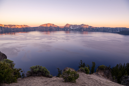 View of the vast serene Crater Lake reflecting the soft hues of the sunset sky embraced by rugged mountainous terrain Crater Lake Oregon United States. View of the vast serene Crater Lake reflecting the soft hues of the sunset sky embraced by rugged mountainous terrain Crater Lake Oregon United States.