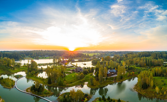 Aerial view of a serene landscape featuring interconnected lakes lush green forests and wooden buildings during a vibrant golden hour sunset in Latvia. Aerial view of a serene landscape featuring interconnected lakes lush green forests and wooden buildings during a vibrant golden hour sunset in Latvia.
