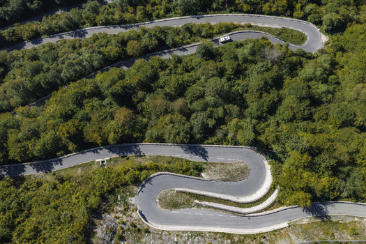 Aerial view of a winding mountain road snaking through a dense green forest in Skofja Loka Slovenia.