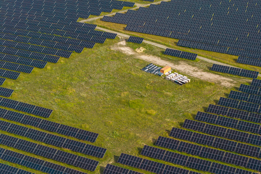 Aerial view of a vast solar farm with rows of photovoltaic panels installed in a green field featuring a small cluster of equipment containers in the center Poland.