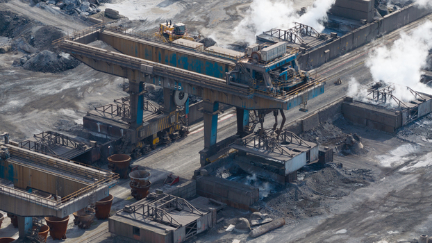 Aerial view of the Tata Steel industrial plant featuring a massive gantry crane rising steam and raw material piles in Velsen Noord Noord Holland Netherlands. Aerial view of the Tata Steel industrial plant featuring a massive gantry crane rising steam and raw material piles in Velsen Noord Noord Holland Netherlands.
