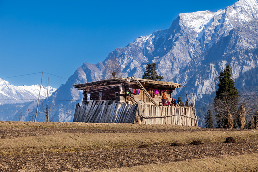 View of a traditional wooden house with people on the porch against the backdrop of snow capped mountains and a clear blue sky in Arang Kel Azad Kashmir Pakistan. View of a traditional wooden house with people on the porch against the backdrop of snow capped mountains and a clear blue sky in Arang Kel Azad Kashmir Pakistan.