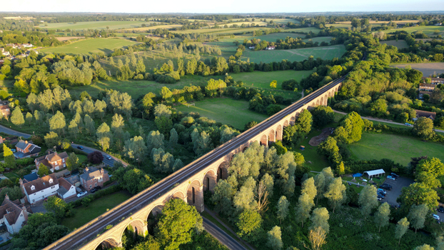 Aerial view of the historic Chappel Viaduct spanning across the lush green countryside with surrounding trees and rural landscape in Chappel England United Kingdom.