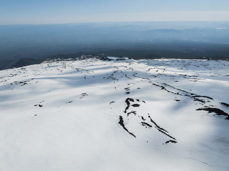 Aerial view of Mount Etna south side with snow covered slopes volcanic craters and dark lava flows under a clear blue sky in Nicolosi Sicilia Italy. Aerial view of Mount Etna south side with snow covered slopes volcanic craters and dark lava flows under a clear blue sky in Nicolosi Sicilia Italy.