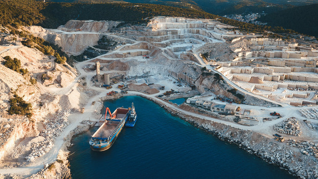 Aerial view of Jadrankamen white stone quarry with a cargo ship being loaded in the bay and terraced excavation sites Pucisca Splitsko dalmatinska Croatia. Aerial view of Jadrankamen white stone quarry with a cargo ship being loaded in the bay and terraced excavation sites Pucisca Splitsko dalmatinska Croatia.