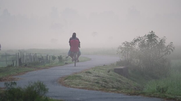 View of people riding a bicycle in foggy Bogura Bangladesh.