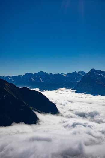Aerial view of the Swiss Alps with rugged mountain peaks rising above a thick sea of clouds under a clear blue sky in Airolo Ticino Switzerland. Aerial view of the Swiss Alps with rugged mountain peaks rising above a thick sea of clouds under a clear blue sky in Airolo Ticino Switzerland.