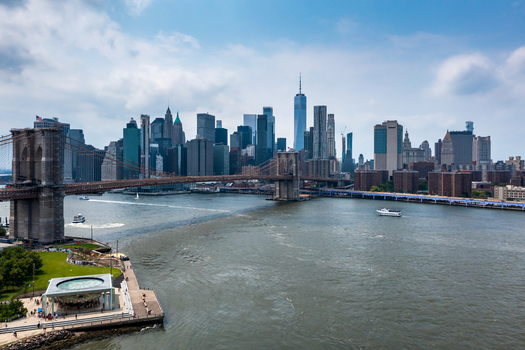 New York United States 11 August 2021 Aerial view of the Brooklyn Bridge spanning the East River with the Manhattan skyline skyscrapers and Jane s Carousel under a blue sky.