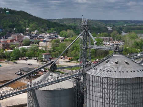 Aerial view of industrial grain silos and conveyor systems with a small town and green hills under a cloudy sky Aurora Indiana United States. Aerial view of industrial grain silos and conveyor systems with a small town and green hills under a cloudy sky Aurora Indiana United States.