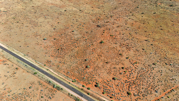 Aerial view of a stark sun baked landscape where ochre earth meets a ribbon of asphalt punctuated by sparse resilient vegetation Karoo Desert Northern Cape South Africa. Aerial view of a stark sun baked landscape where ochre earth meets a ribbon of asphalt punctuated by sparse resilient vegetation Karoo Desert Northern Cape South Africa.